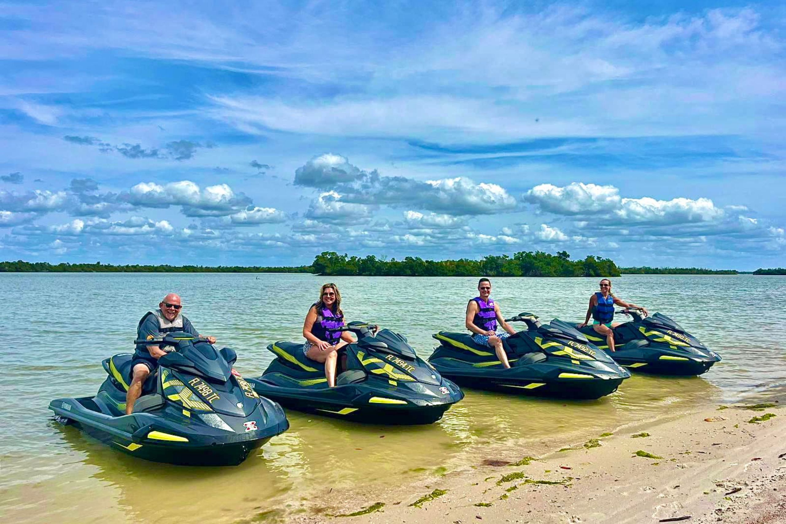 group of four jet skiers on jet skis pulled up to the shore of a beach